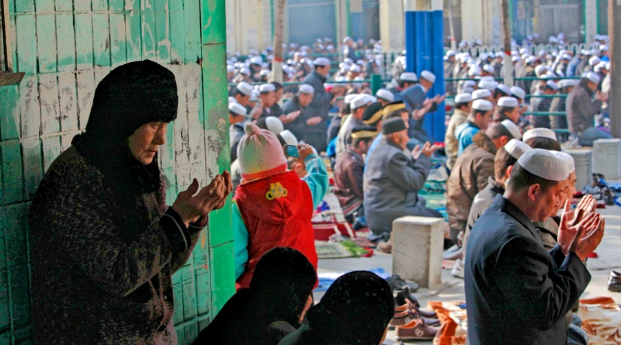 An elderly Muslim woman in Xining, Qinghai Province, performs prayer alone in a small alley beside the street during Eid al-Adha